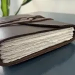 leather bound handmade journal with jagged page edges resting on a blue dresser