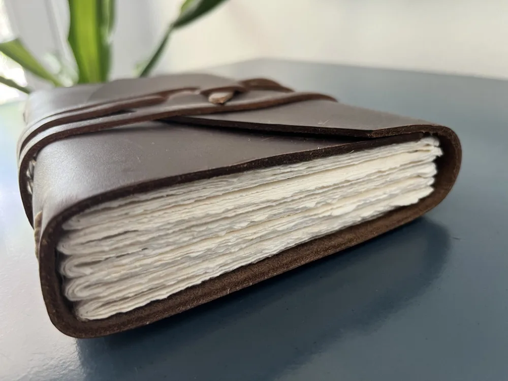 leather bound handmade journal with jagged page edges resting on a blue dresser