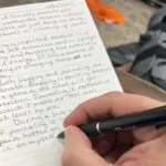 image of a hand holding a pen, writing in a journal about the difference between blogging and journaling