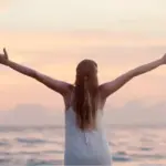 woman standing arms outstretched before the ocean at sunset