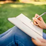 woman sitting on the grass while writing in a journal